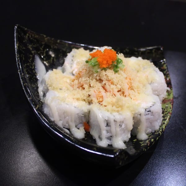 Sushi rolls topped with crunchy tempura flakes, orange roe, and green onions on a decorative plate.