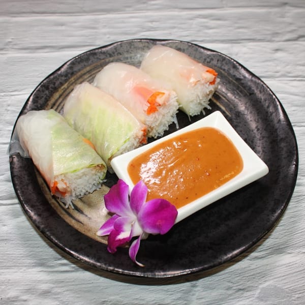 Four fresh spring rolls with peanut sauce and an orchid on a dark plate.
