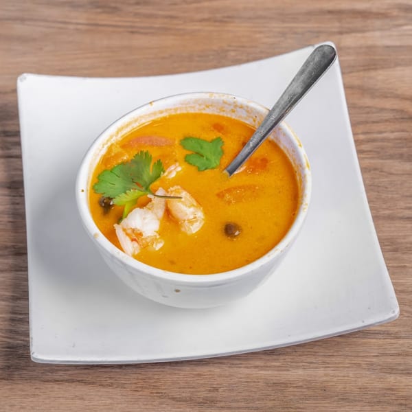 A white bowl of Chaba Thai Restaurant's Tom Yum soup with shrimp and cilantro on a white plate.